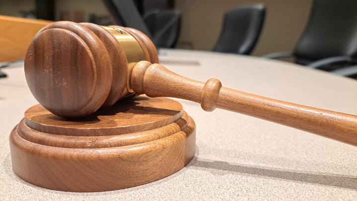 A wooden gavel rests on its sound block in the foreground, with council chamber chairs visible in the background.