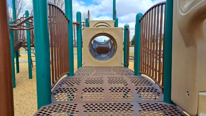  A close up view of a playground structure with a bridge, railings, and a tunnel.